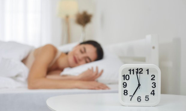 woman sleeping behind alarm clock