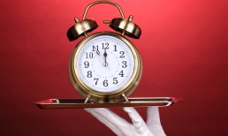 white-gloved hand with alarm clock on tray